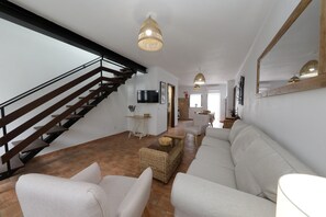 A modern living room with a staircase, white sofas, and a wooden coffee table.