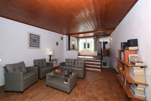 A living room with wicker furniture, a coffee table, a bookshelf, and a staircase leading to another room.