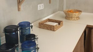 A kitchen counter with storage jars, a wicker basket, and a shelf with mugs.