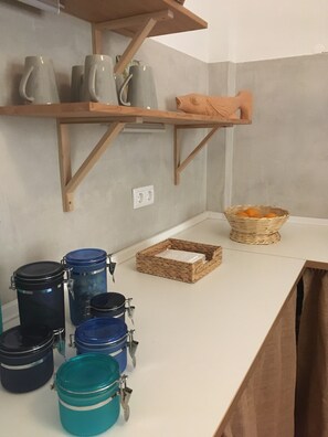 A kitchen counter with storage jars, a wicker basket, and a shelf with mugs.
