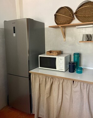 A kitchenette with a stainless steel refrigerator, a microwave, and a small shelf with baskets and containers.