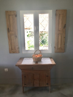 A room with a wooden table, a basket of oranges, and a window with shutters.