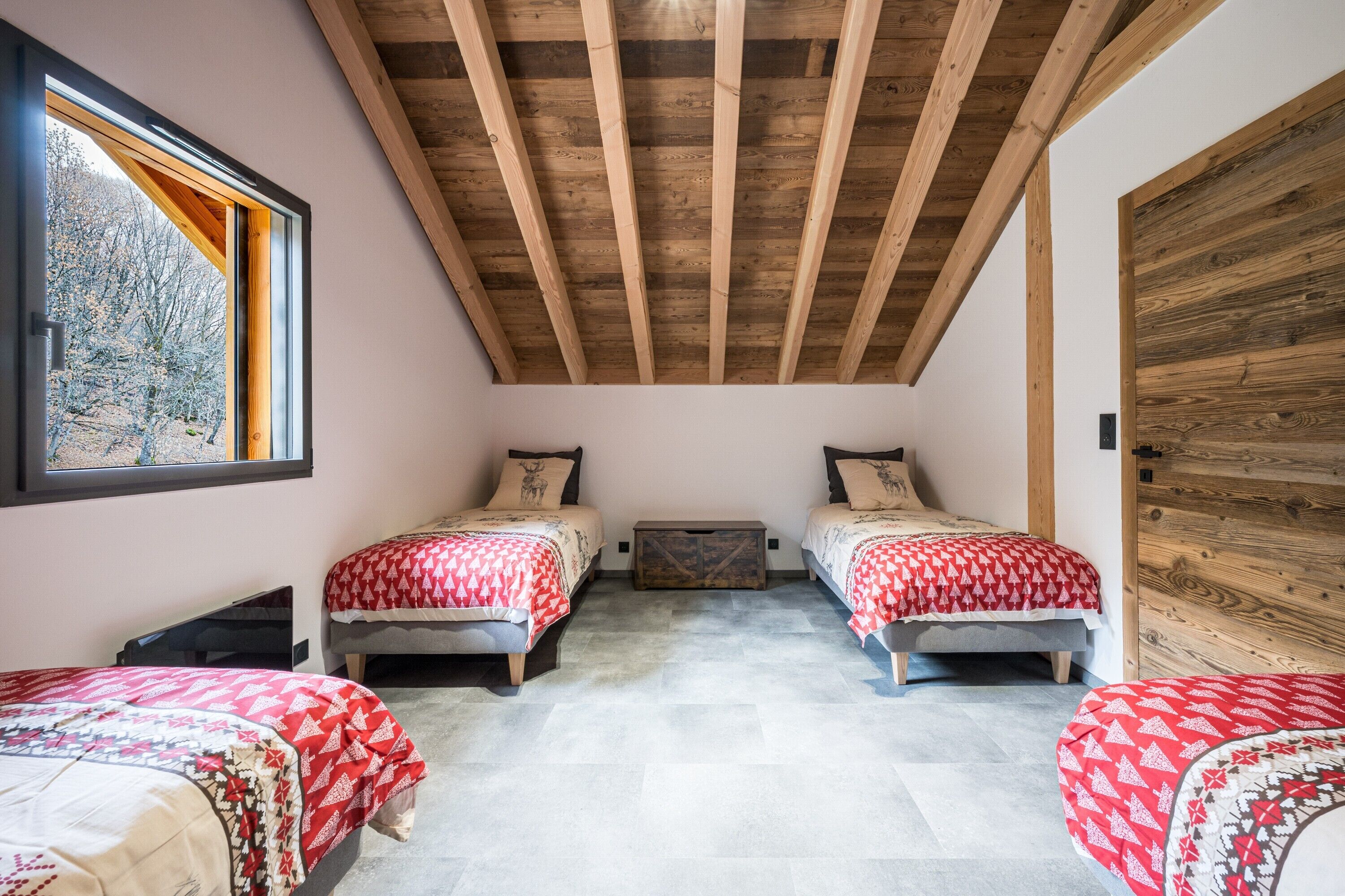 Une chambre avec deux lits, des poutres apparentes en bois au plafond, une fenêtre donnant sur la forêt et un mur en bois.