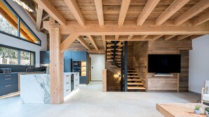 Amplia sala de estar con cocina, una escalera de madera y un televisor grande.