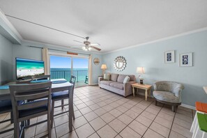 Ein Wohnzimmer mit Fernseher, Deckenventilator, einer Couch, einem Sessel und Blick auf den Ozean.