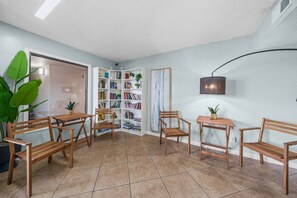 Ein Zimmer mit Bücherregal, Holzstühlen, einem Tisch und einer Wandlampe.