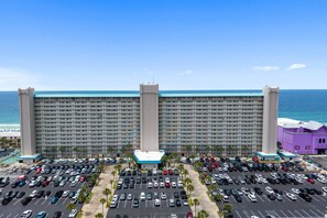 A large hotel with a parking lot in front, a beach view, and a clear sky.