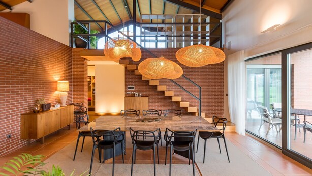 Un espace de salle à manger moderne, doté d’une grande table, de chaises et de luminaires suspendus.