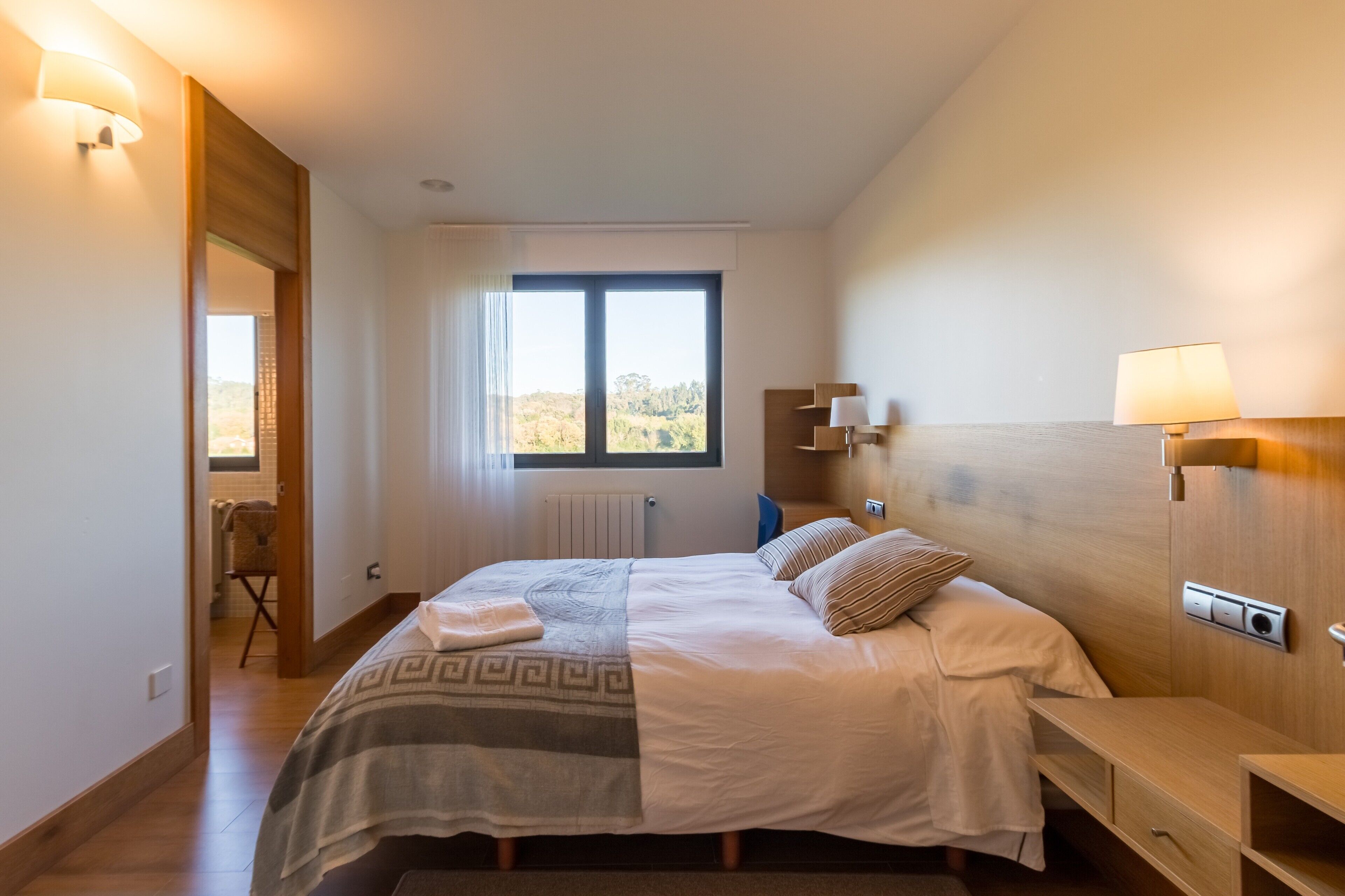 Ein Schlafzimmer mit einem Bett, Nachttischen, einem Fenster und Blick ins Freie.
