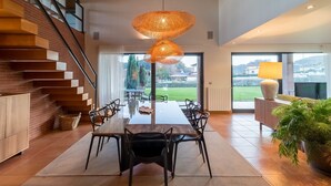 Un espace de salle à manger moderne avec un escalier en bois, une grande table à manger et un luminaire suspendu.