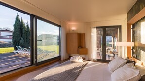 Une chambre avec un grand lit, une vue sur l’extérieur, une armoire en bois et une porte en verre donnant sur un patio.