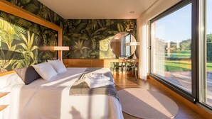 Une chambre à coucher avec un grand lit, une vue sur l’extérieur, une tête de lit en bois et un petit bureau avec une chaise.