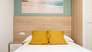 A bed with two pillows, a nightstand, a wall-mounted power outlet, and a painting of a beach scene.