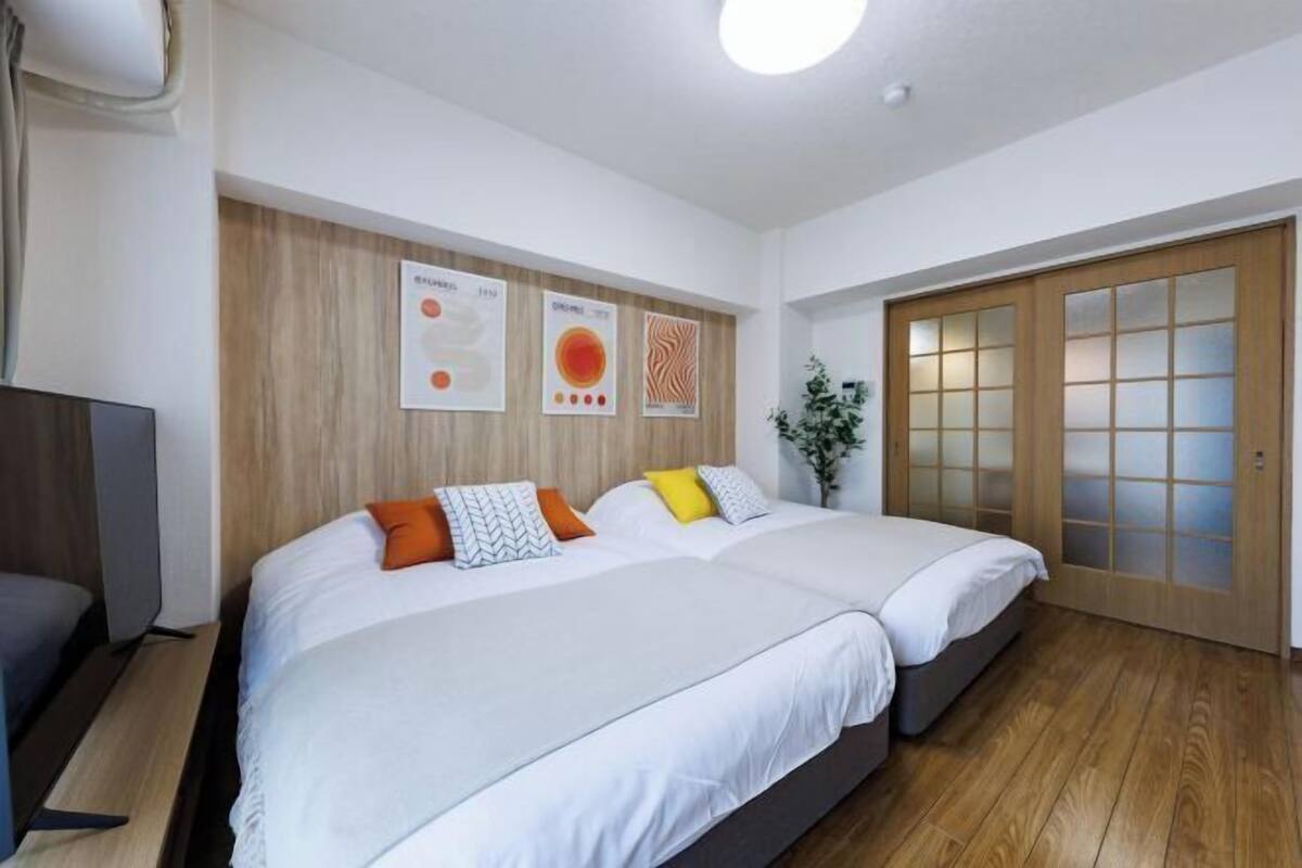 A hotel room with two beds, a wooden floor, a TV, and a sliding door with frosted glass panels.
