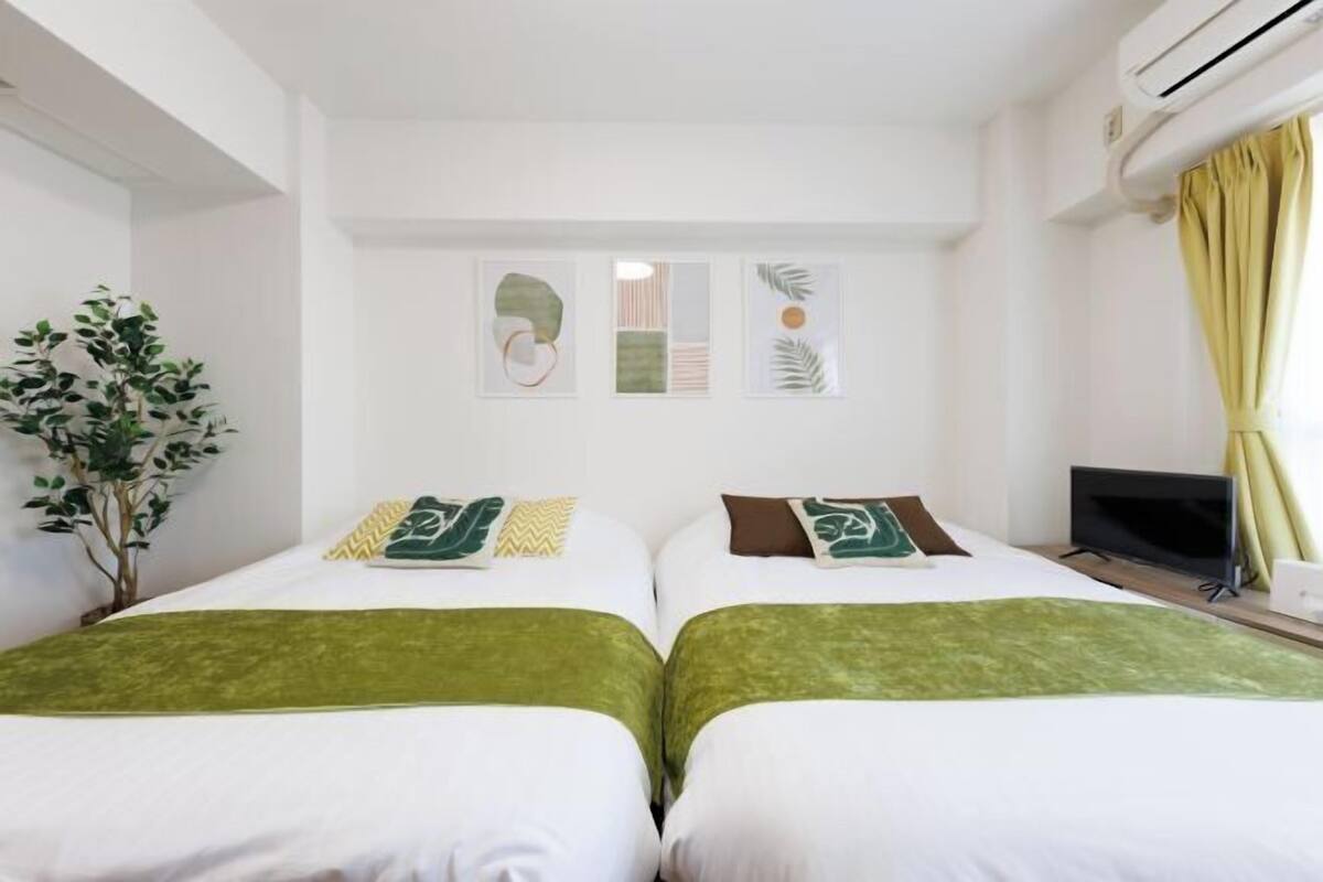 A hotel room with two beds, a TV, and a plant.