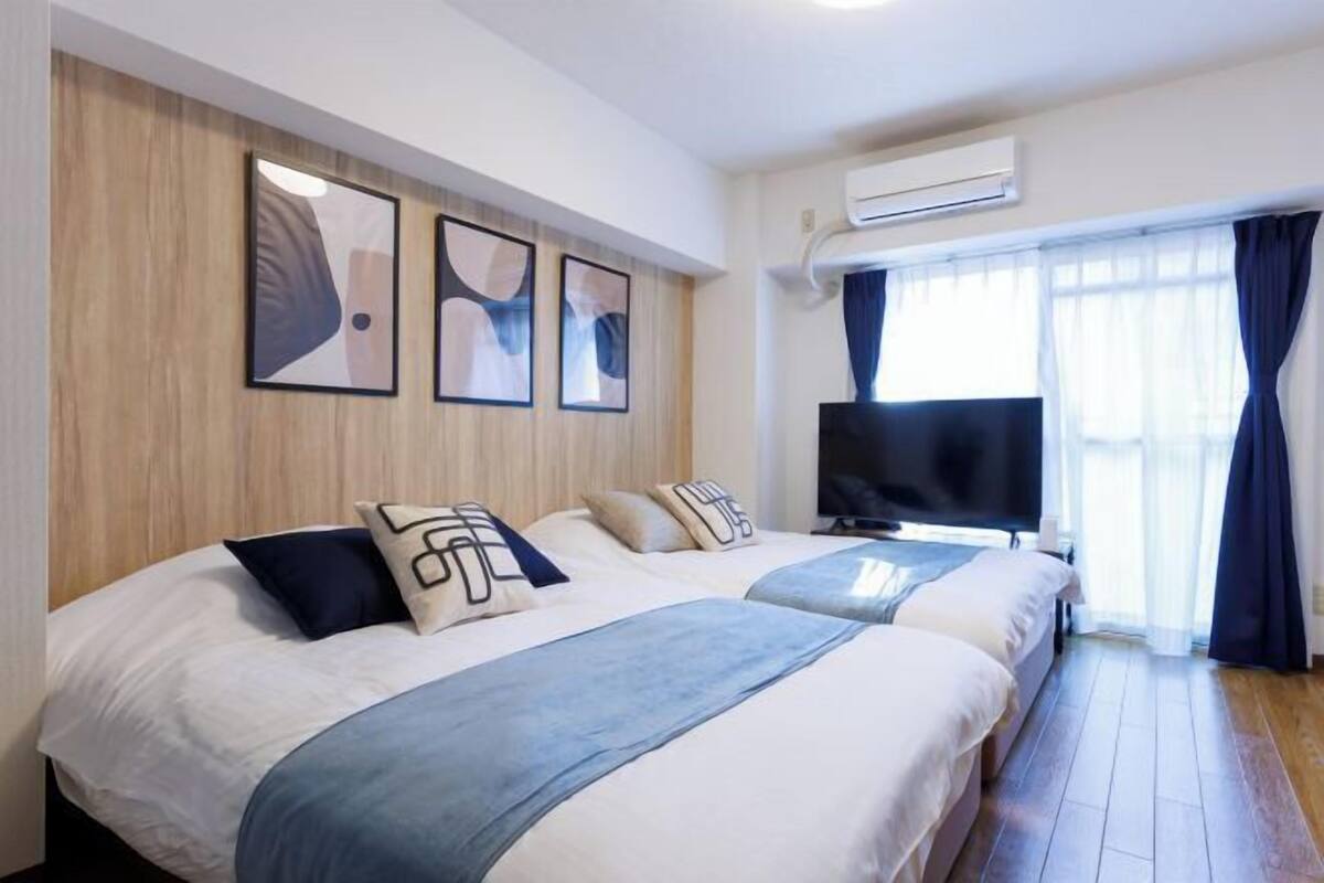 A hotel room with two beds, a flat-screen TV, and a large window with curtains.