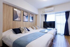 Habitación de hotel con dos camas, televisión de pantalla plana y un ventanal grande con cortinas.