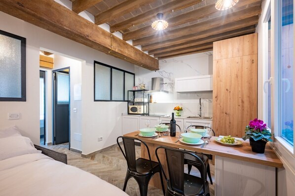A modern kitchen with wooden beams, a dining area with chairs, and a view through a window.