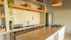 A modern kitchen with a central island, wooden shelves, and hanging plants. - Casinha Praia do Espelho (Porto Seguro)