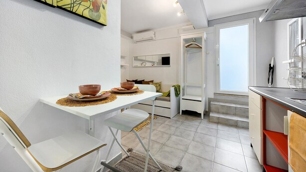 A modern kitchen with white cabinetry, a dining area with a white table and chairs, and a large window providing natural light. - Studio Apartment 'Economy  For Two in Lagos' with Shared Pool, Wi-Fi and Air Conditioning (Lagos)