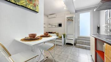 A modern kitchen with white cabinetry, a dining area with a white table and chairs, and a large window providing natural light.