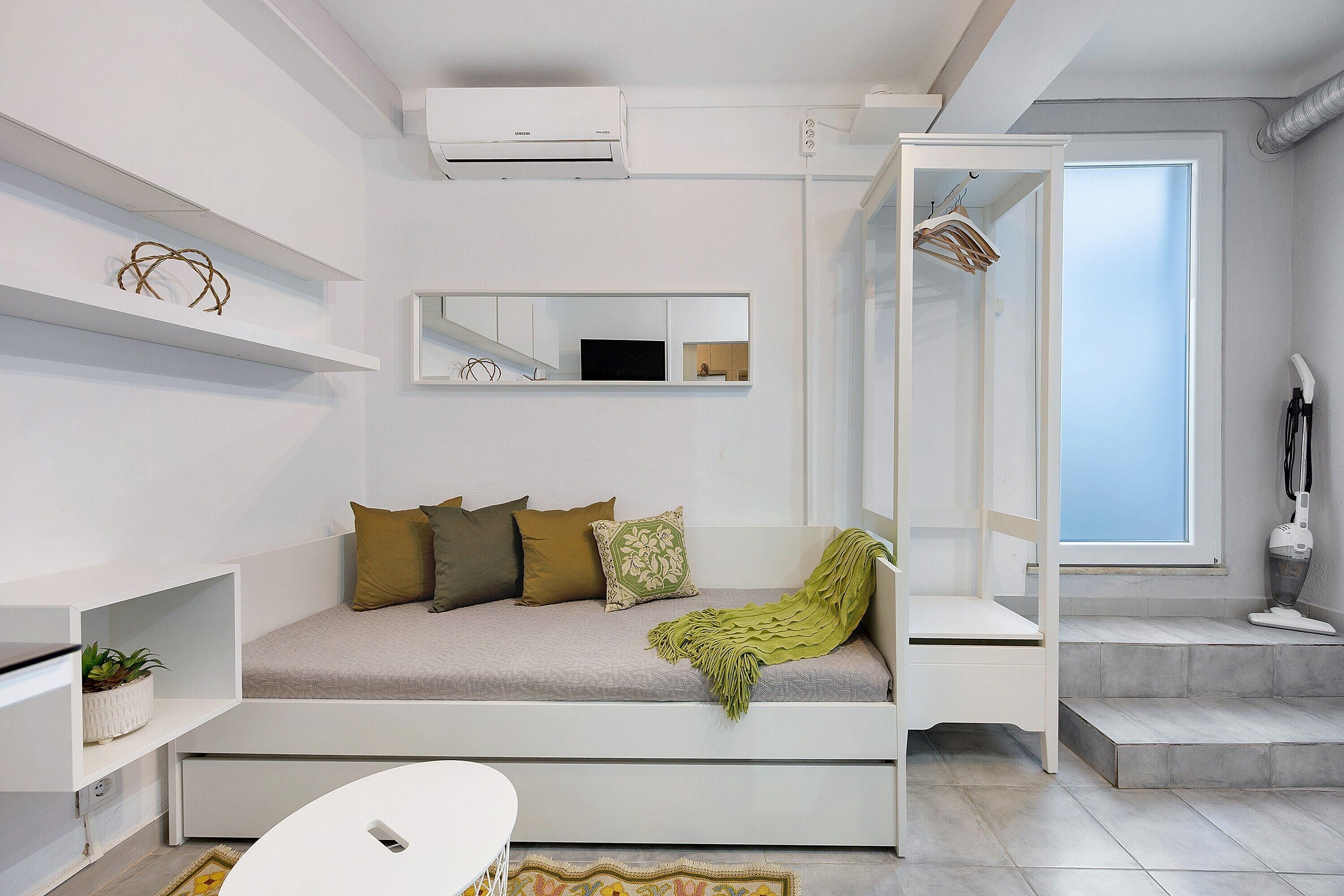 A modern room with a sofa bed, a small table, a mirror, and a window.