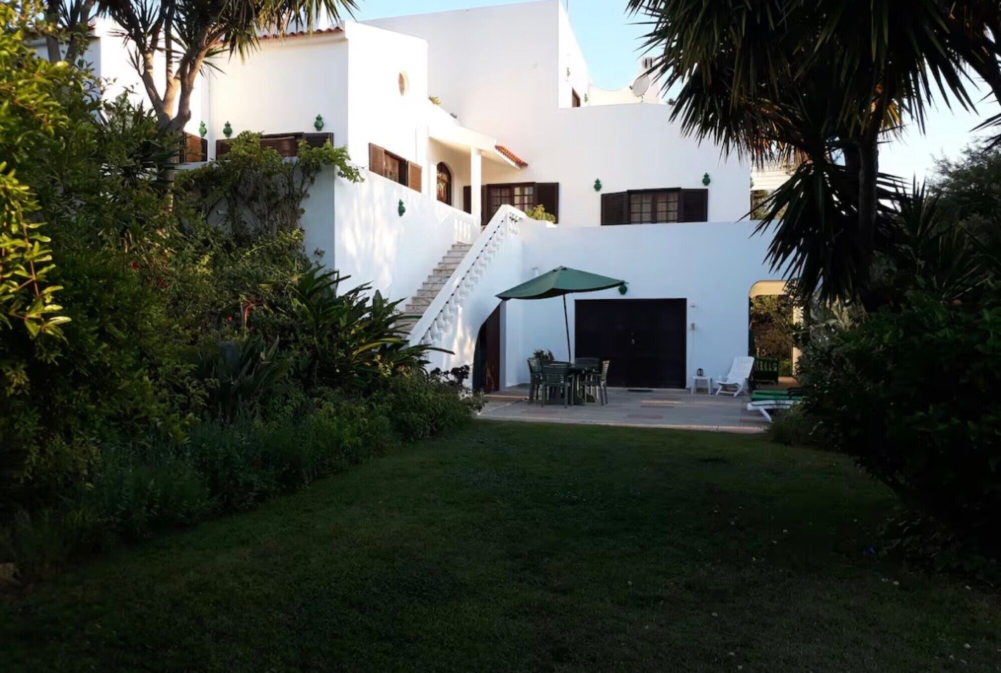 A white building with a staircase, a covered patio with chairs, and a garage door.