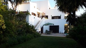 A white building with a staircase, a covered patio with chairs, and a garage door. - Studio Apartment 'Economy  For Two in Lagos' with Shared Pool, Wi-Fi and Air Conditioning (Lagos)