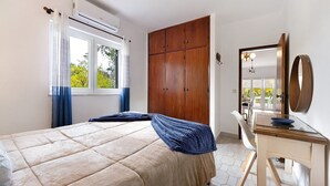 Une chambre à coucher avec un lit, une armoire en bois, un bureau avec un miroir et une fenêtre avec des rideaux.