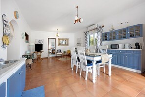 A spacious kitchen with blue cabinets, a dining table with white chairs, and a large window. - Apartment 'Tranquility Villa Fonte Coberta' with Shared Pool, Wi-Fi and Air Conditioning (Lagos)