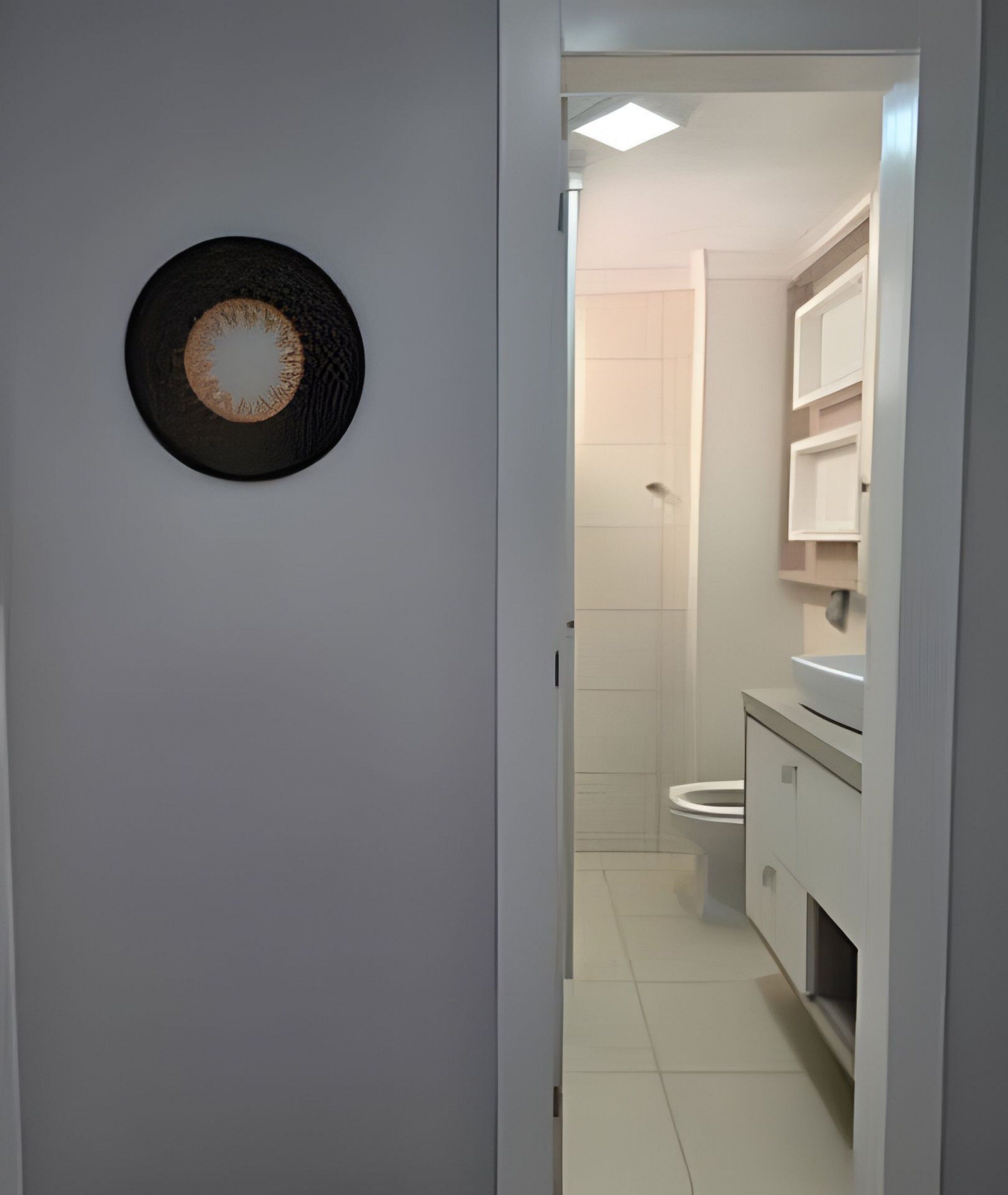 A narrow hallway leading to a bathroom with a toilet, a sink, and a mirror.