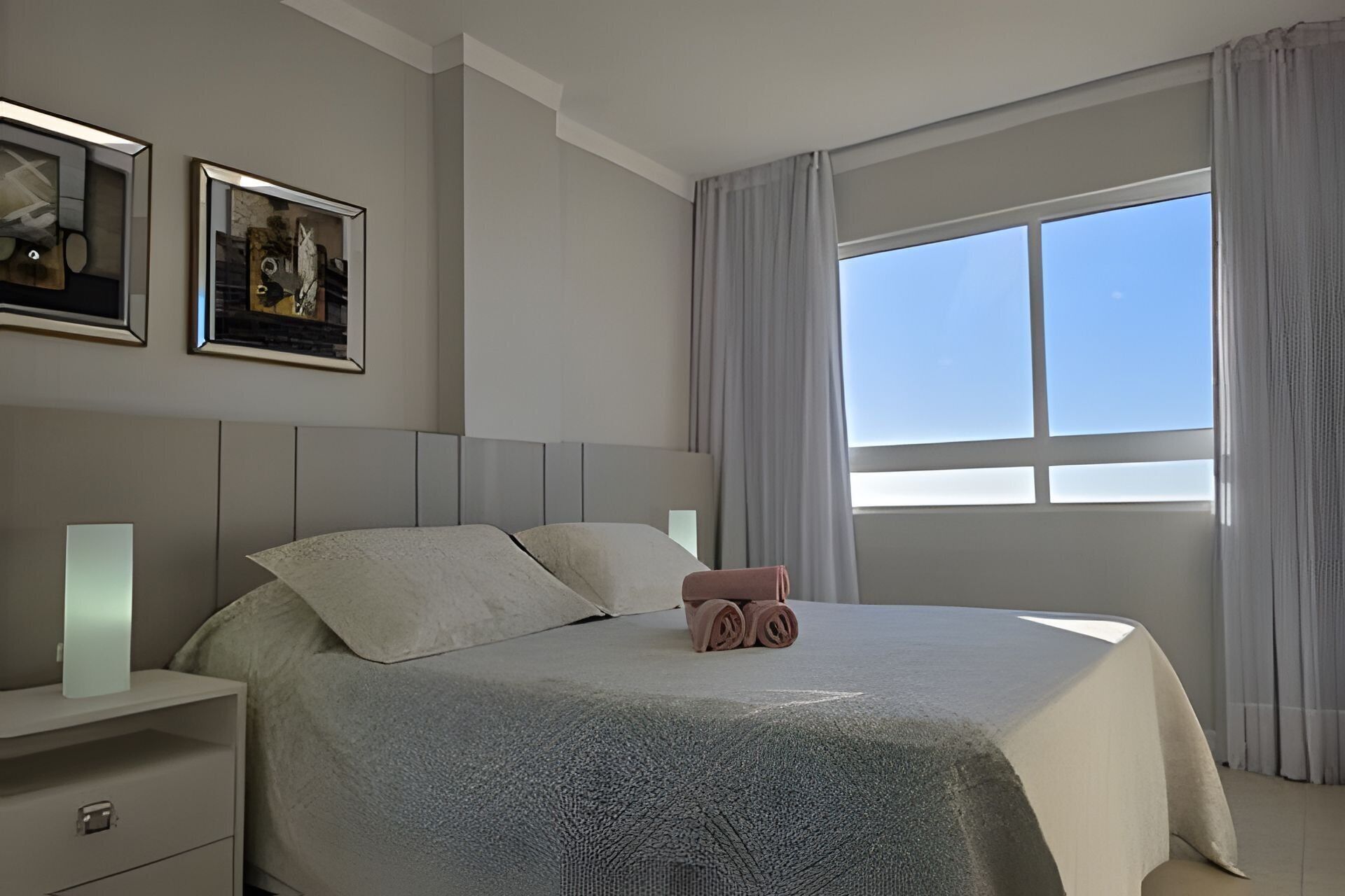 Una habitación de hotel moderna con una cama grande, una mesita de noche y un ventanal con cortinas.