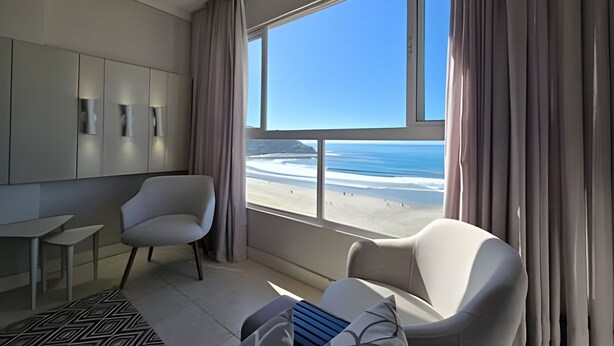 Une chambre d’hôtel moderne dotée d’une grande fenêtre donnant sur la plage et l’océan.