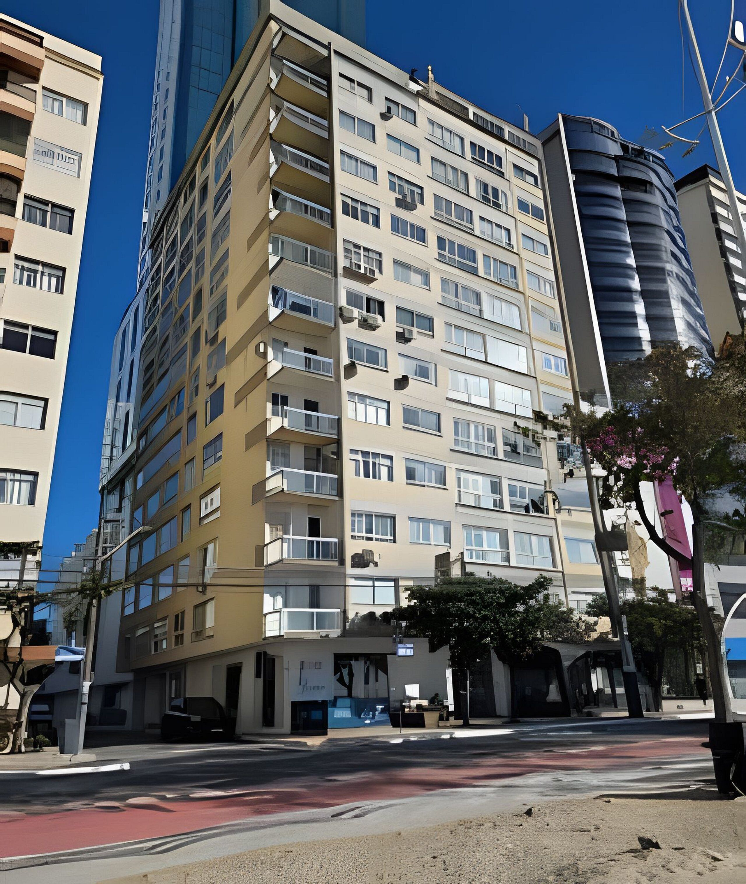 Un edificio de varios pisos con balcones, entrada a nivel de calle y un cielo azul despejado.