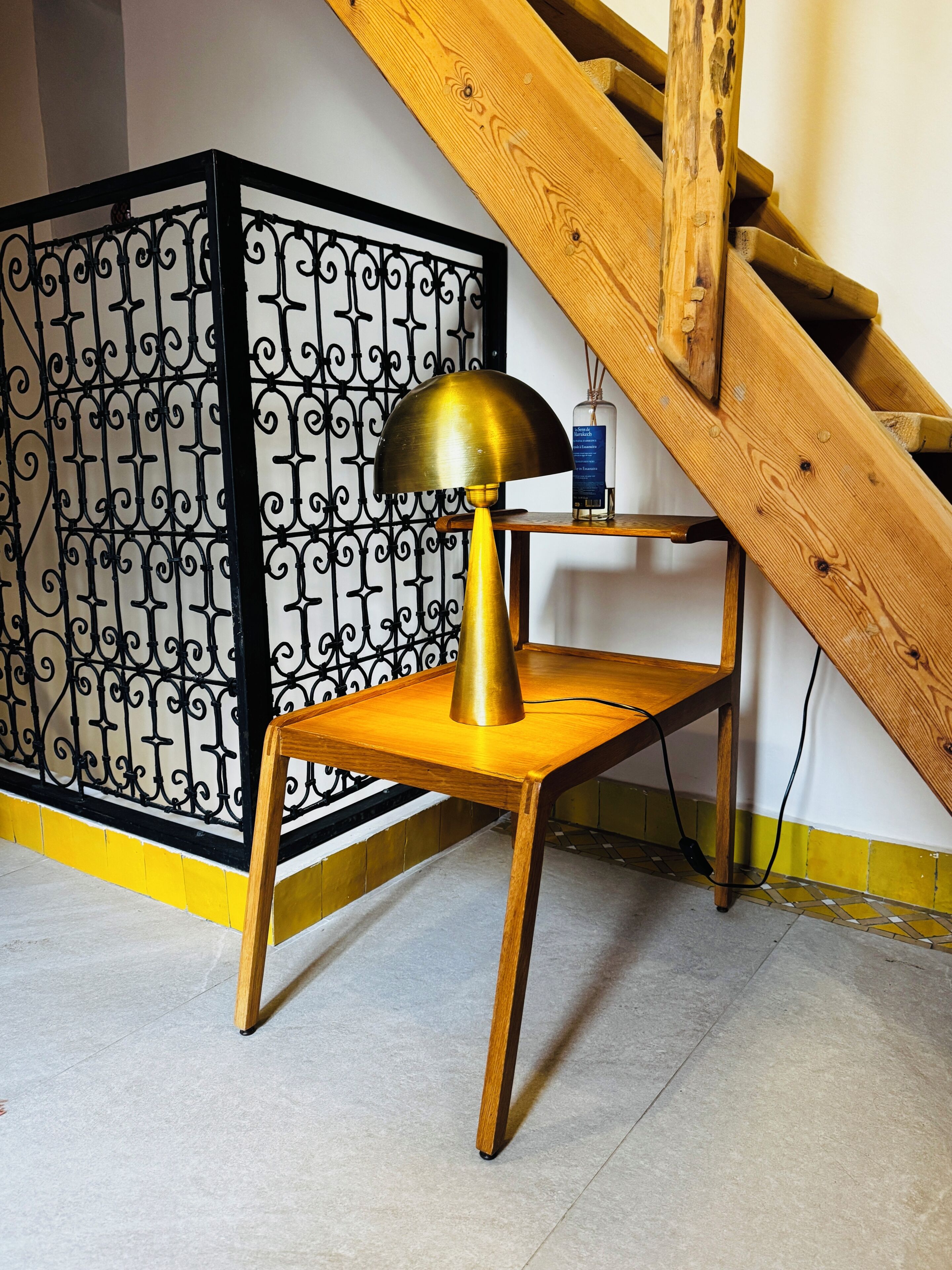 A wooden chair with a brass lamp, a wooden table, and a staircase with a wooden railing.