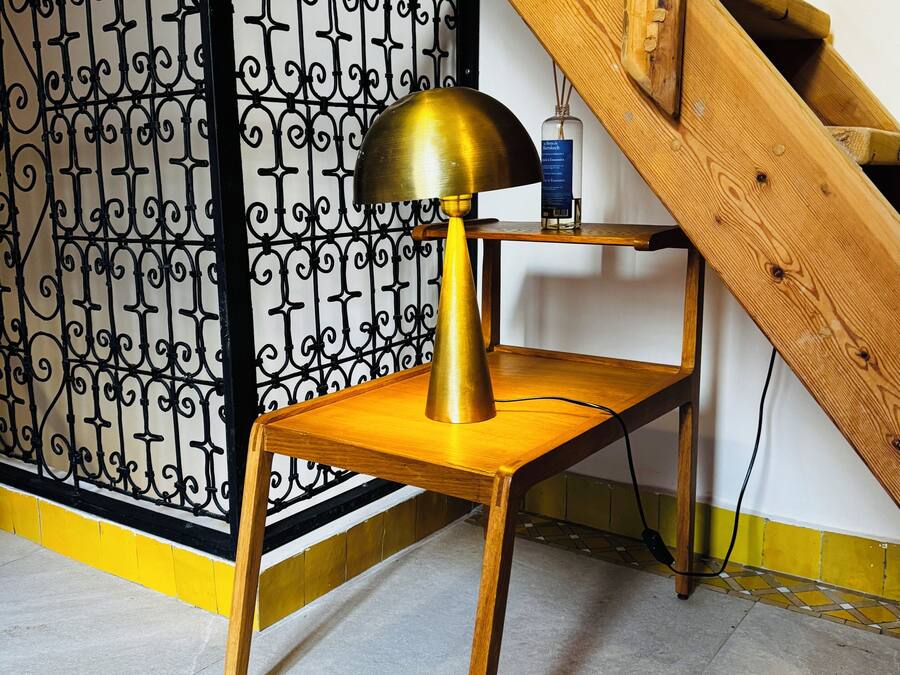 A wooden chair with a brass lamp, a wooden table, and a staircase with a wooden railing.