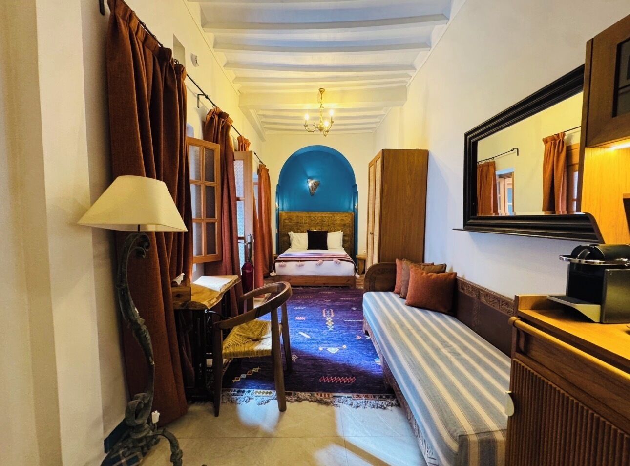 Una habitación de hotel con cama, sofá, escritorio, lámpara y espejo.
