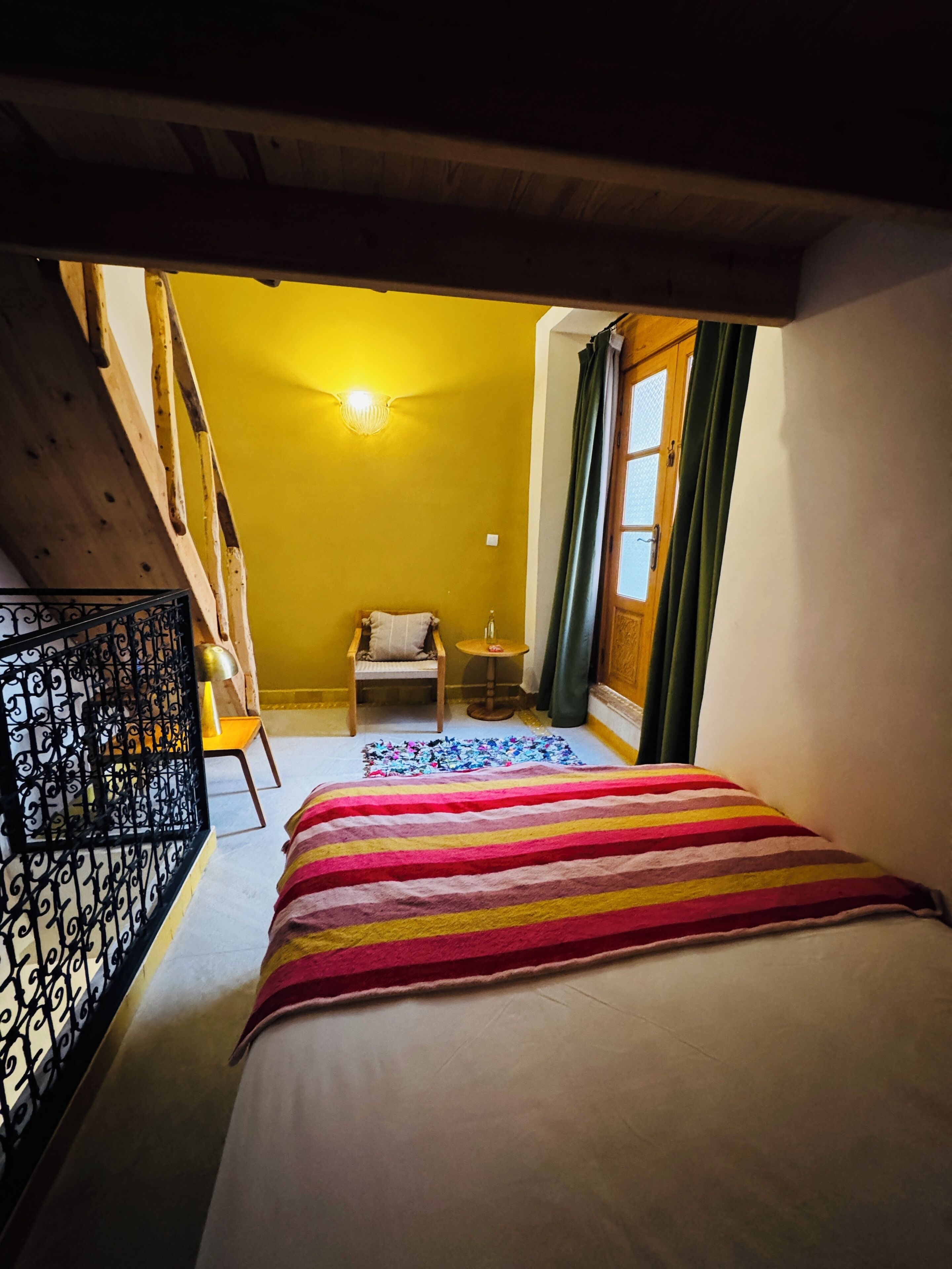 A bedroom with a bed, a chair, a small table, and a window with curtains.