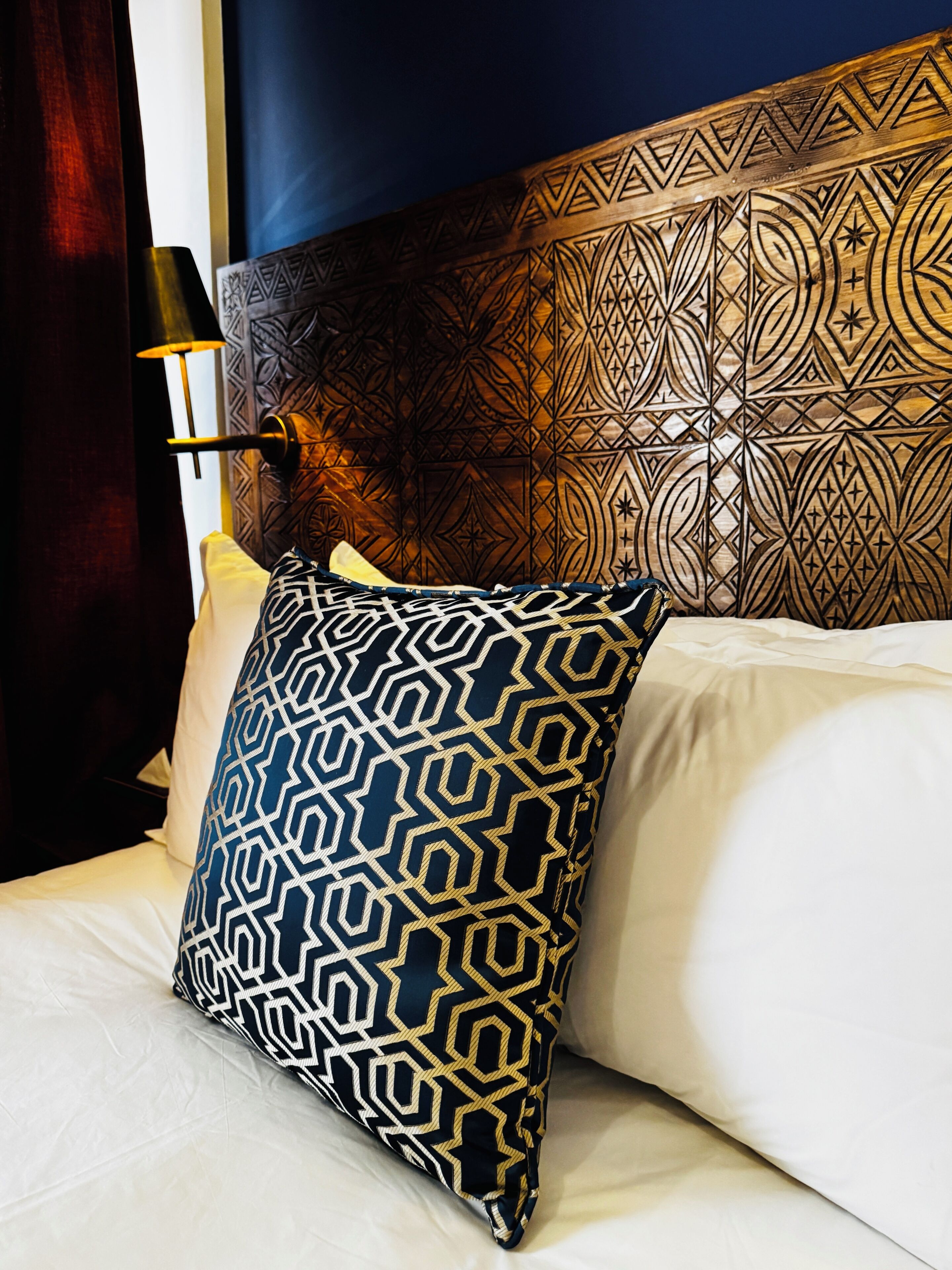 A bed with a patterned pillow, a headboard with intricate designs, and a bedside lamp.