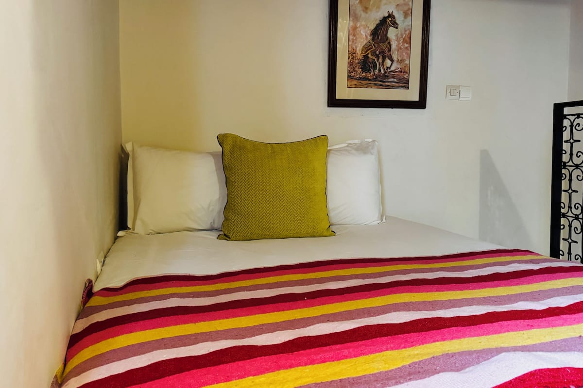 A bed with a striped blanket, two pillows, and a framed picture on the wall.