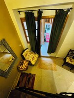 A room with a large mirror, a floral sofa, a chessboard, and a view through a doorway to a balcony with potted plants.