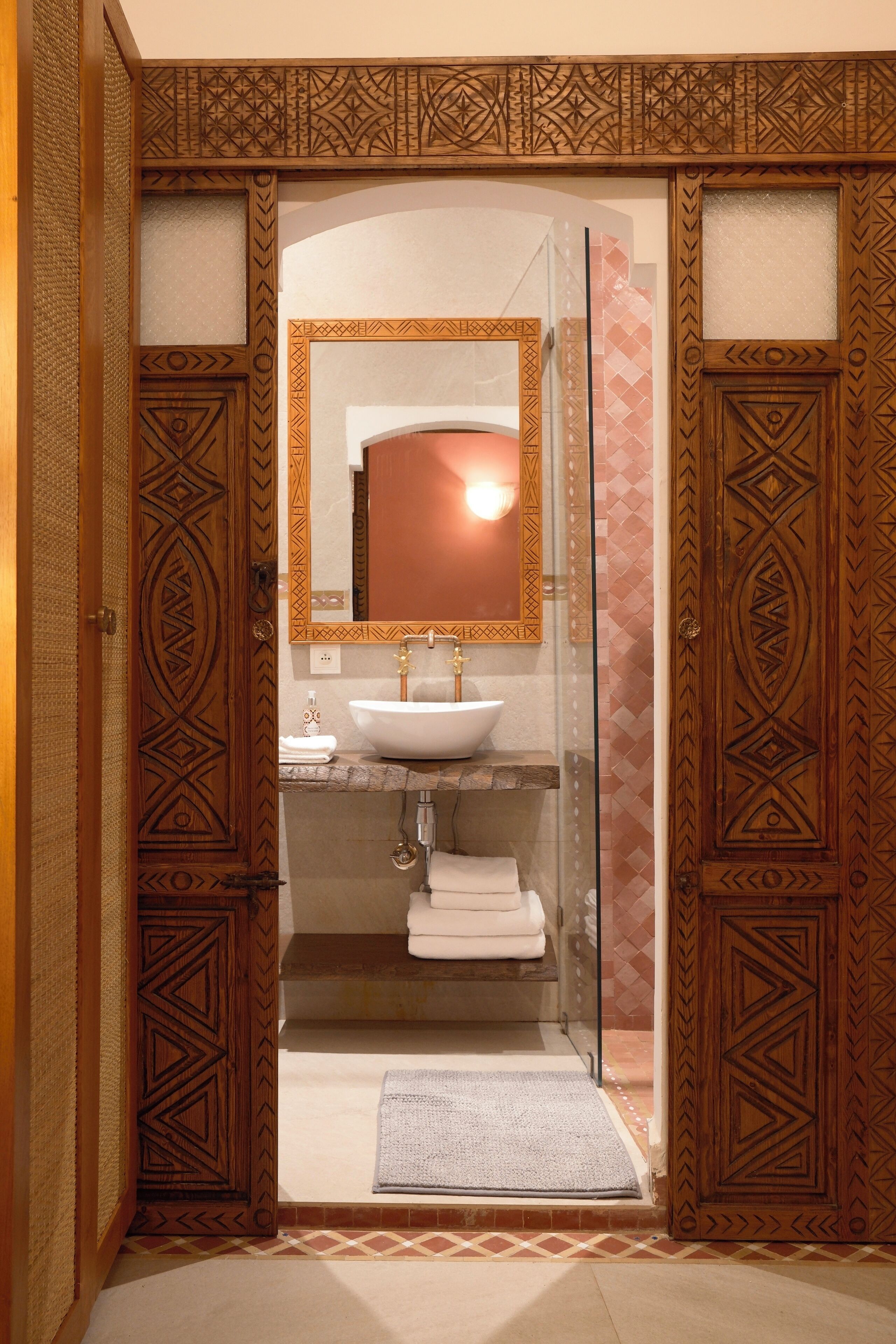A bathroom with a wooden door, a glass shower enclosure, a white sink, and a mirror with a decorative frame.