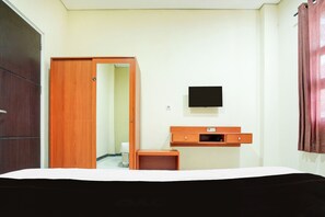 A hotel room with a bed, a wooden wardrobe, a small wooden table, a TV mounted on the wall, and a door leading to another room. - OYO 94806 Kostel 97 (Palembang)