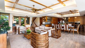 A spacious living area with a high ceiling, wooden beams, a central seating area with a coffee table, and a dining set.