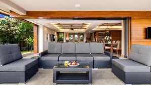 A modern living room with a sectional sofa, a glass coffee table, and a dining area visible through an open door.