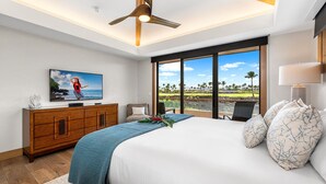 A modern hotel room with a large bed, a wooden dresser, a television, and a view of a tropical landscape.
