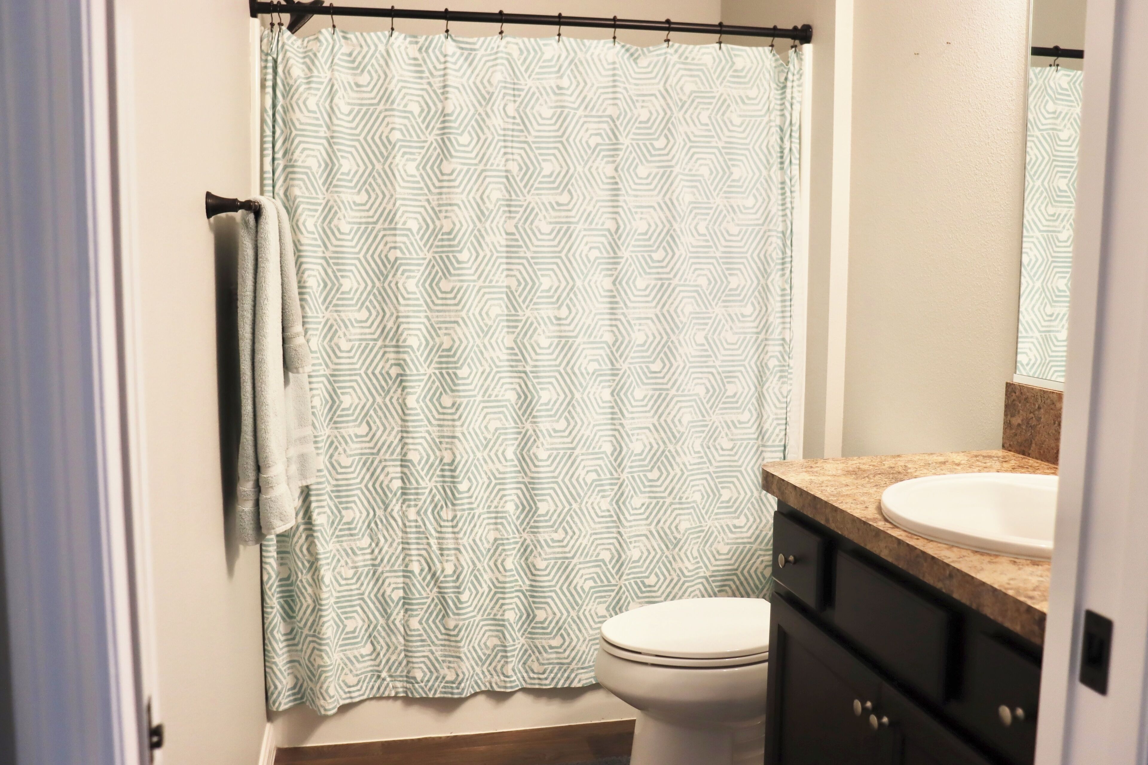 A bathroom with a patterned shower curtain, a white toilet, a sink with a granite countertop, and a mirror above the sink.