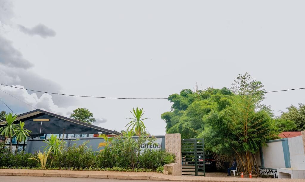 A building with a sign that reads "GITEGO" and a gated entrance with a person sitting on a bench.