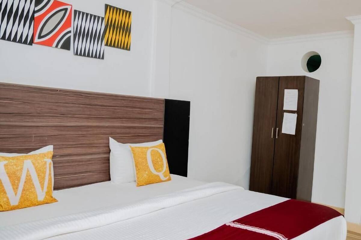 A neatly made bed with white and red bedding, two pillows with letters, a wooden headboard, and a wardrobe with papers on it.