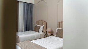 A hotel room with two beds, a bedside table with a lamp, and a large window with curtains. - Igitego Hotels (Kigali)